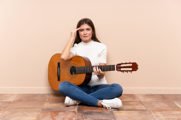 Mujer joven con guitarra sentado en el suelo infeliz y frustrado con algo. Expresión facial negativa
