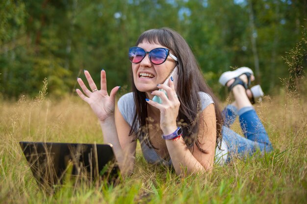 Mujer joven hablando emocionalmente el teléfono y mirando a un ordenador portátil mujer autónoma trabaja en un