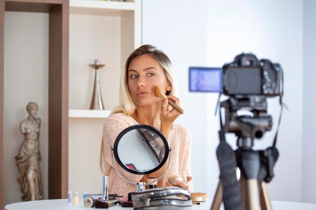 Mujer joven hablando sobre cosméticos sosteniendo una paleta de maquillaje mientras graba su video Mujer haciendo un video para su blog sobre cosméticos