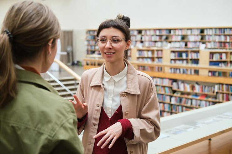 Mujer joven hablando con su amiga mientras están parados en la biblioteca