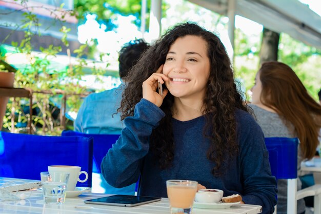 Mujer joven hablando por teléfono móvil en la cafetería.