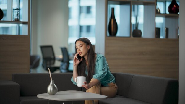 Mujer joven hablando por teléfono móvil en el lugar de trabajo interior mujer llamando por teléfono celular