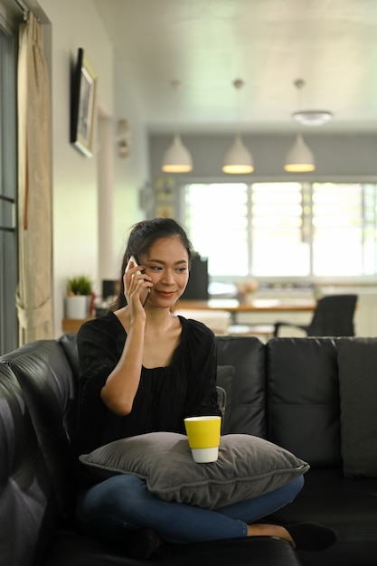 Foto una mujer joven está hablando por un teléfono móvil mientras está sentada en un sofá de cuero