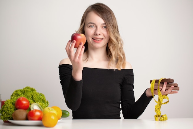 La mujer joven hace una elección entre alimentos saludables y no saludables.