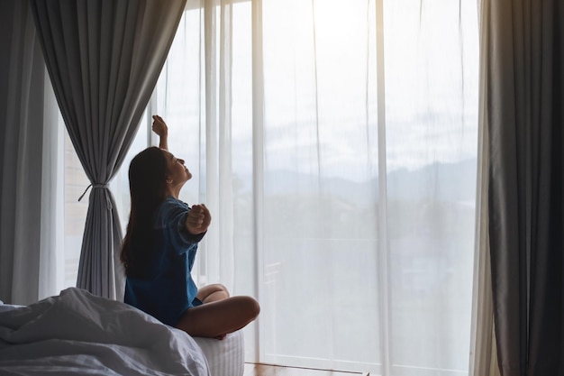 Una mujer joven hace estiramientos después de despertarse por la mañana en una acogedora cama blanca en casa