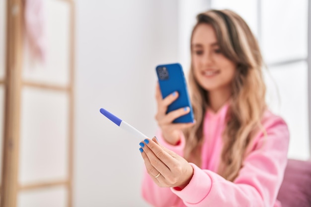 Mujer joven hace foto por teléfono inteligente para prueba de embarazo en el dormitorio