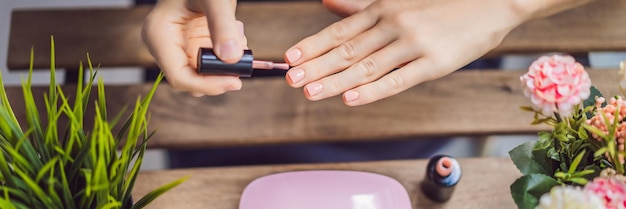 Mujer joven hace manicura con esmalte de gel y lámpara uv en formato largo de banner de tonos rosas