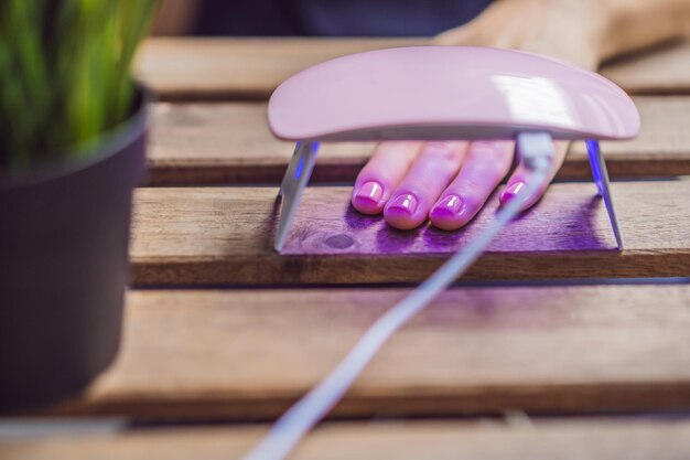 Mujer joven hace manicura con esmalte de gel y lámpara UV en tonos rosas