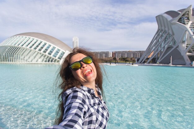 Mujer joven hace selfie en el fondo del edificio Hemisferic en la Ciudad de las Artes y las Ciencias en Valencia, España.