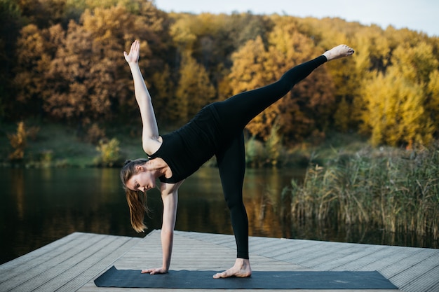 Mujer joven haciendo asanas de yoga en la naturaleza cerca del lago