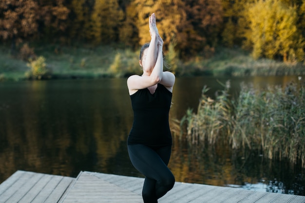 Mujer joven haciendo asanas de yoga en la naturaleza cerca del lago