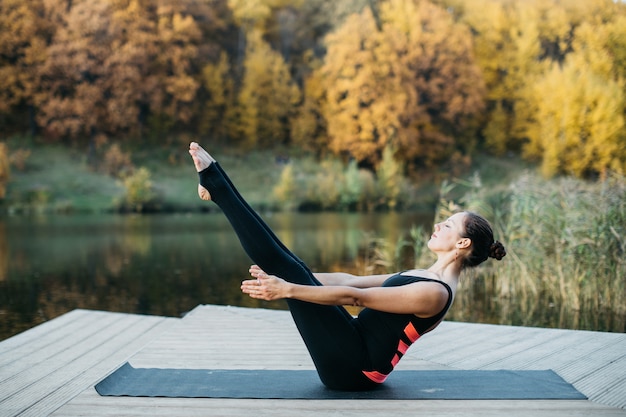 Mujer joven haciendo asanas de yoga en la naturaleza cerca del lago