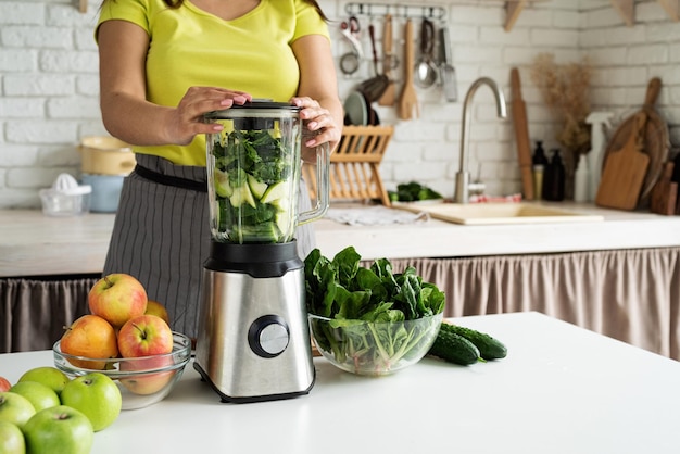 Mujer joven haciendo batido verde en la cocina de casa