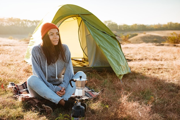 Mujer joven haciendo café al aire libre cerca de una carpa