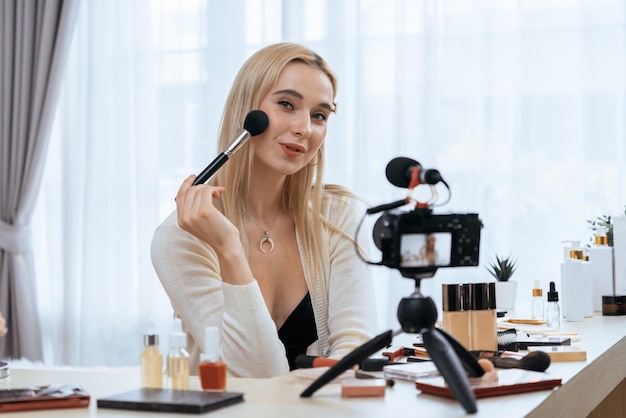 Mujer joven haciendo contenido de video tutorial de belleza y cosméticos para redes sociales Blogger de belleza sonríe a la cámara mientras muestra cómo aplicar máscara a la audiencia o seguidores Blithe.