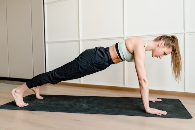 Mujer joven haciendo deporte en estera de yoga en casa