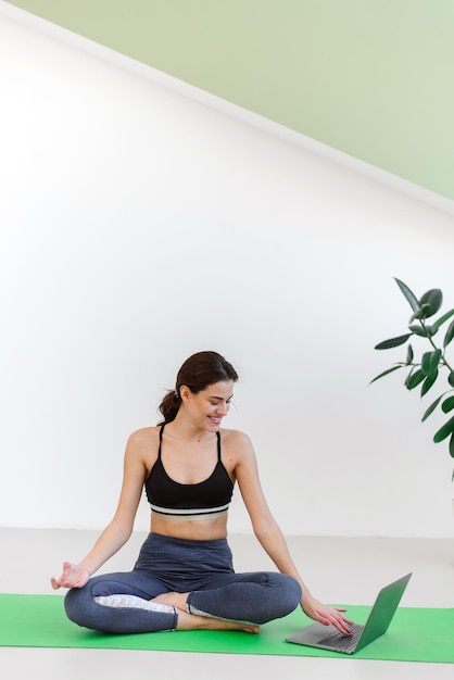 Mujer joven haciendo deportes y yoga en casa usando una computadora portátil Publicidad para cursos de yoga