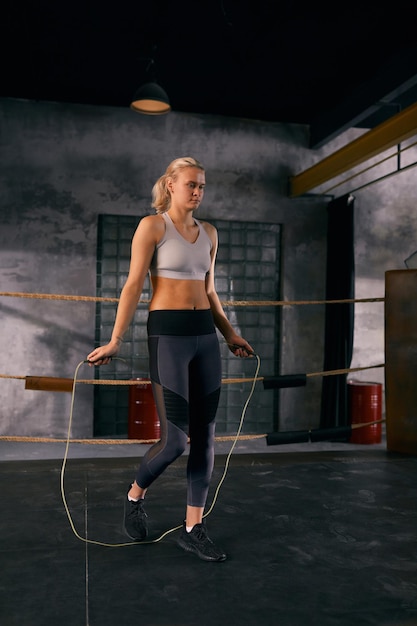 Mujer joven haciendo ejercicio de calentamiento de cuerda de saltar antes de boxear en ring cuadrado