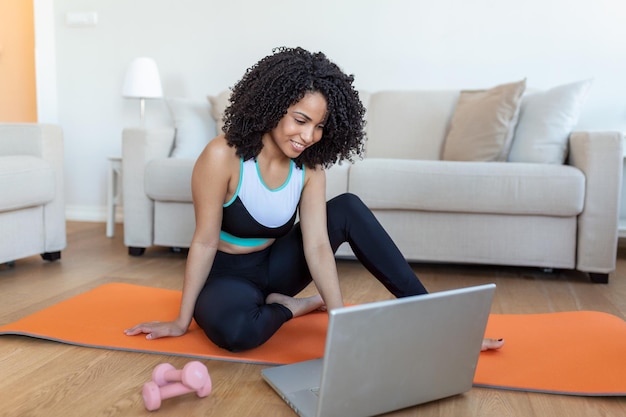 Mujer joven haciendo ejercicio en casa en una sala de estar Lección en video Mujer joven repitiendo ejercicios mientras ve una sesión de entrenamiento en línea Hermosa mujer joven haciendo ejercicio físico en casa