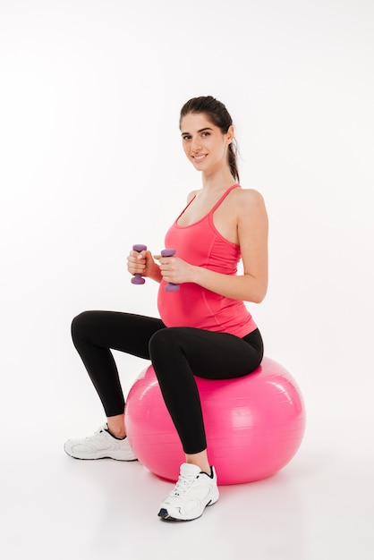 Mujer joven haciendo ejercicio de embarazo con pelota de fitness y pesas