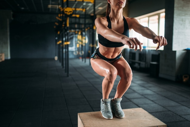 Mujer joven haciendo ejercicio de salto de caja en el gimnasio. Entrenamiento de la atleta femenina atractiva en el gimnasio