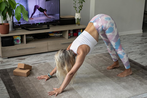 Mujer joven haciendo ejercicio de yoga en línea en casa viendo tutorial en la pantalla de televisión