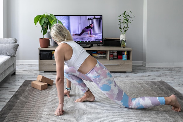 Mujer joven haciendo ejercicio de yoga en línea en casa viendo tutorial en la pantalla de televisión
