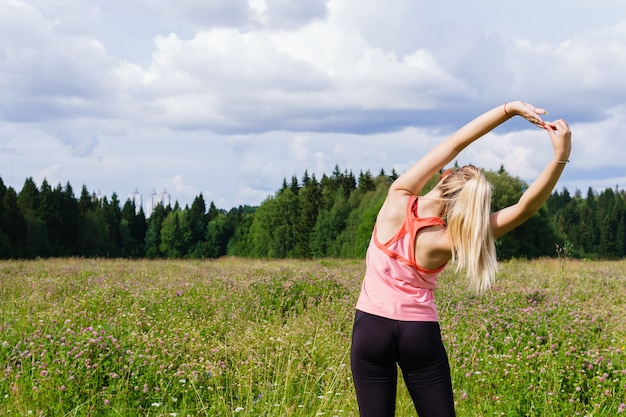 Mujer joven haciendo ejercicios de estiramiento de los brazos al aire libre en un prado en las afueras de la ciudad