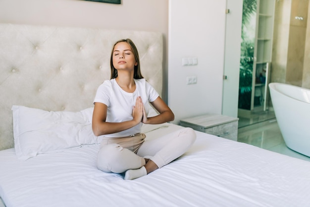 Mujer joven haciendo ejercicios de yoga en la cama en casa