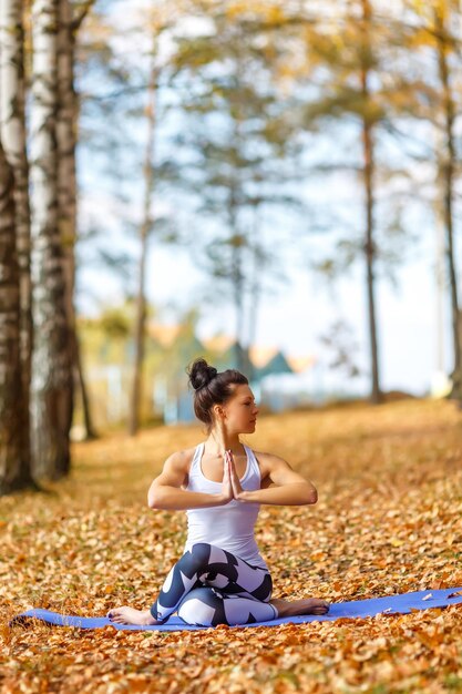 Mujer joven haciendo ejercicios de yoga en el concepto de estilo de vida de salud del parque de la ciudad de otoño