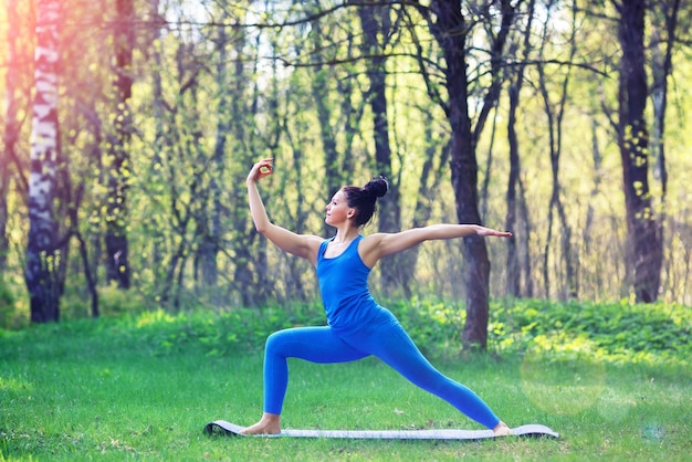 Mujer joven haciendo ejercicios de yoga en el concepto de estilo de vida de salud del parque de la ciudad de verano