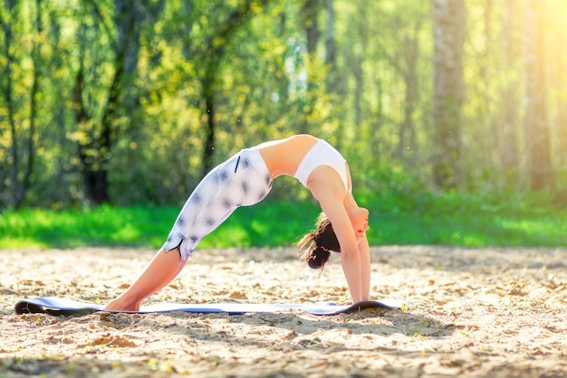 Mujer joven haciendo ejercicios de yoga en el concepto de estilo de vida de salud del parque de la ciudad de verano