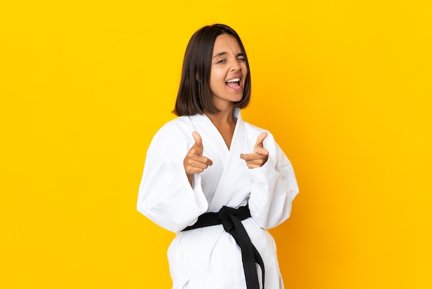 Mujer joven haciendo karate aislado sobre fondo amarillo apuntando hacia el frente y sonriendo