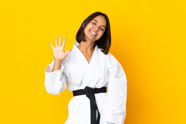 Mujer joven haciendo karate aislado sobre fondo amarillo contando cinco con los dedos