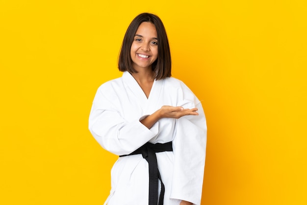 Mujer joven haciendo karate aislado sobre fondo amarillo presentando una idea mientras mira sonriendo hacia