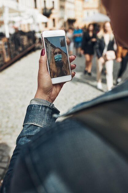 Foto mujer joven haciendo una llamada de video hablando mientras camina por el centro de la ciudad por la noche usando la máscara facial