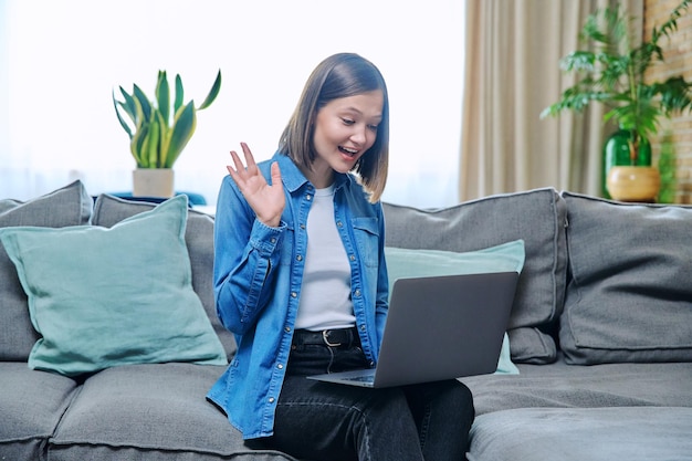 Mujer joven haciendo una llamada de video sentada en el sofá en casa agitando usando una computadora portátil