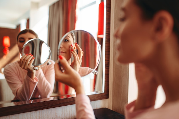 Foto mujer joven haciendo maquillaje frente al espejo en el dormitorio.