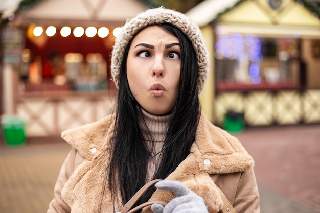 Mujer joven haciendo muecas mientras está de pie en la feria de vacaciones de invierno