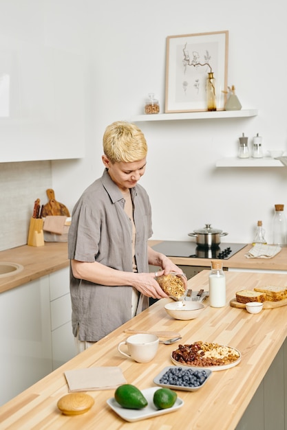 Mujer joven haciendo muesli para el desayuno en la mesa de la cocina