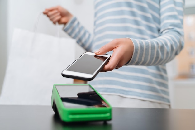 Mujer joven haciendo pagos móviles con su teléfono inteligente en la tienda