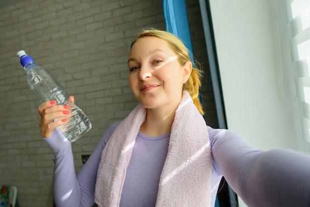 Mujer joven haciendo selfies después del ejercicio. Sonriente mujer atractiva fitness con toalla y botella de agua después del entrenamiento.