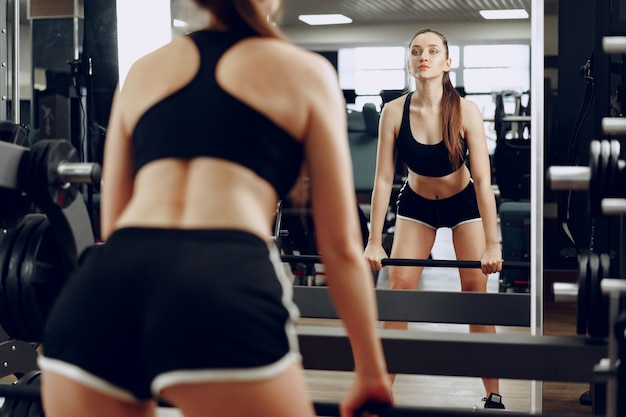 Mujer joven haciendo sentadillas con barra en un aparato de gimnasio