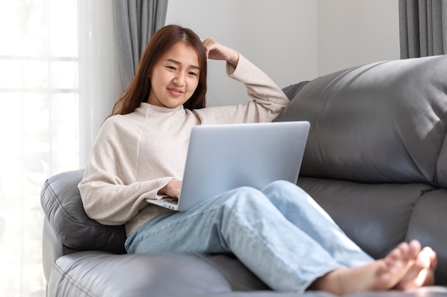 Mujer joven haciendo trabajo de investigación para su negocio, sonriente mujer sentada en el sofá relajante mientras navega por el sitio web de compras en línea