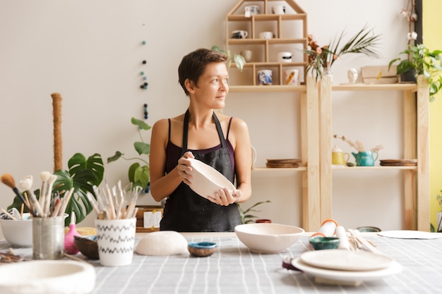 Mujer joven haciendo vajilla de cerámica y alfarería en el taller