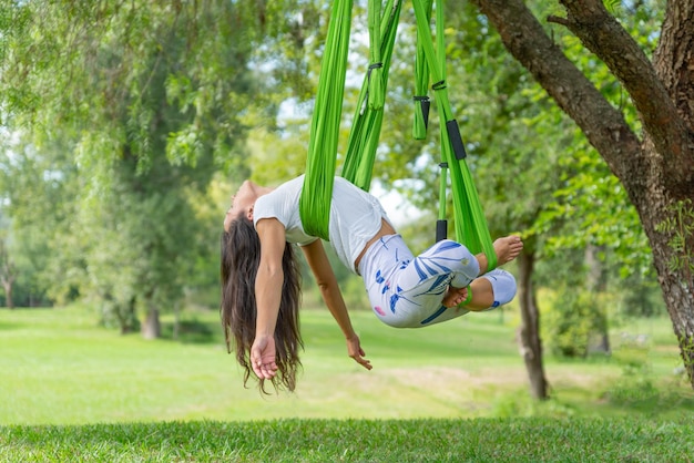 Mujer joven haciendo yoga antigravedad en un parque en un día soleado