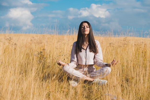 Mujer joven haciendo yoga en el campo de trigo