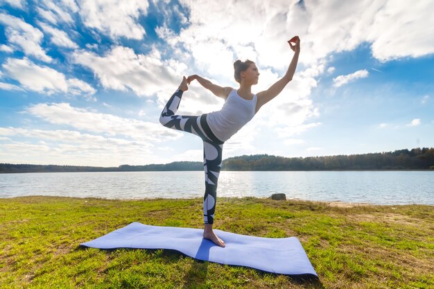 Mujer joven haciendo yoga cerca del lago al aire libre, meditación. Fitness deportivo y ejercicio en la naturaleza. Puesta de sol de otoño.