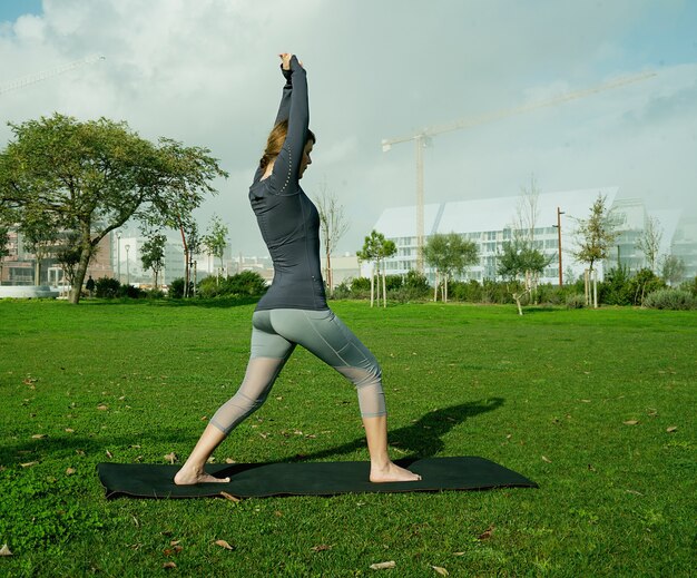 Mujer joven haciendo yoga, estiramiento, ejercicio, entrenamiento en el parque con estera de yoga. Presentación de yoga natural para principiantes. Concepto de salud.