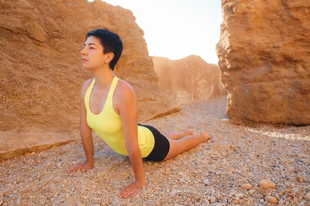 Foto mujer joven haciendo yoga entre las rocas en la playa.